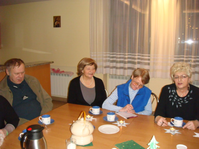 Czterej ludzie siedzą przy stole z porcelanowymi filiżankami i papierowymi dekoracjami świątecznymi.