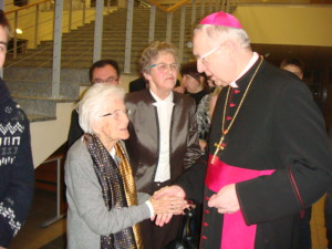 Biskup w stroju liturgicznym wita kobiety podczas wydarzenia w galerii, w tle widoczne schody.