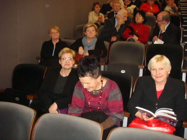 Grupa osób siedzi w widowni teatru lub sali koncertowej, w rzędach krzeseł.