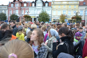 Tłum ludzi zgromadzony na placu miejskim, w tle budynki z czerwonymi dachami.