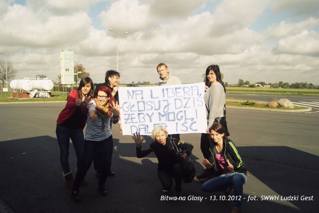 Grupa osób trzyma transparent z hasłem „Na Liberę dziś, żeby mogli i dalej iść” na tle drogi i nieba.