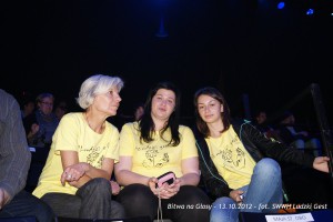 Trzy osoby w żółtych koszulkach siedzą razem podczas wydarzenia „Bitwa na Głosy” w 2012 roku.