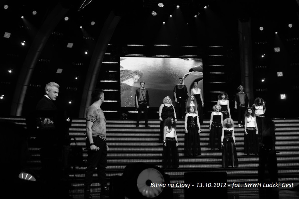 Grupa osób na scenie, oświetlona reflektorami, w kontekście wydarzenia „Bitwa na Głosy” z 13.10.2012.