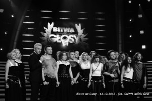 Grupa osób stoi na scenie przed logiem programu „Bitwa na Głosy”, data: 13.10.2012.