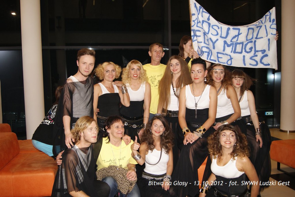 Grupa osób stoi przed budynkiem, trzymając transparent z napisem. Bitwa na Głosy, 13.10.2012.