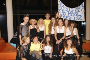 Grupa osób stoi przed budynkiem, trzymając transparent z napisem. Bitwa na Głosy, 13.10.2012.