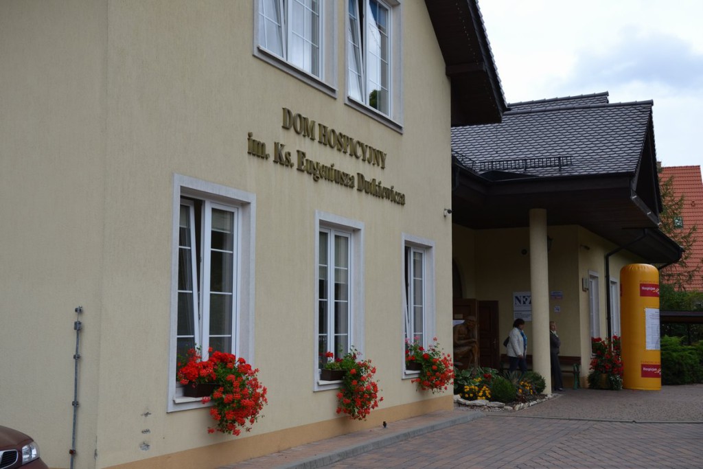 Dom Hospicyjny im. ks. Eugeniusza Dutkiewicza, widok elewacji z kwiatami w donicach i zadaszeniem wejścia.
