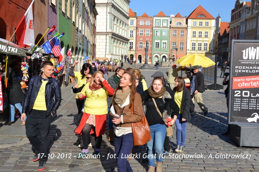 Grupa osób idzie brukowaną ulicą w Poznaniu, w tle kolorowe kamienice i flagi.