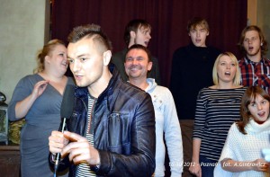 Mężczyzna z mikrofonem stoi przed grupą osób w pomieszczeniu.
