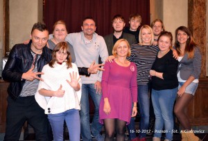Grupa osób stoi razem, pozując do fotografii w pomieszczeniu z ciemnym tłem, wykonanej 16 października 2012 w Poznaniu.