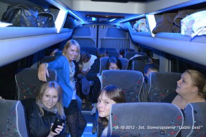 Grupa osób podróżuje autobusem z niebieskim oświetleniem, widoczne siedzenia i wnętrze pojazdu.