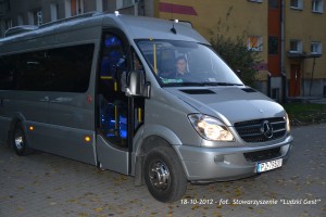 Szary bus z napisem zaparkowany przed budynkiem.