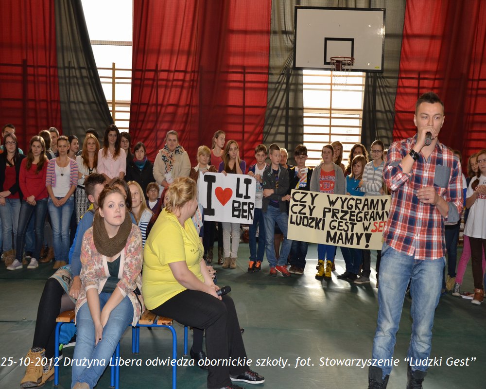 Grupa osób z transparentami uczestniczy w spotkaniu w szkolnej sali gimnastycznej, 25.10.2012.