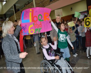Drużyna Libera wita uczniów w obornickiej szkole, w tle grupa dzieci z transparentami.