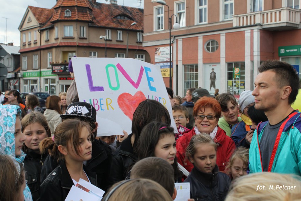 Uczestnicy wydarzenia trzymają transparent z napisem „Love Liber”, w tle widoczne budynki i tłum ludzi.