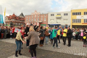 Tłum ludzi uczestniczy w plenerowym wydarzeniu na brukowanym placu, w tle widoczne zabytkowe budynki.