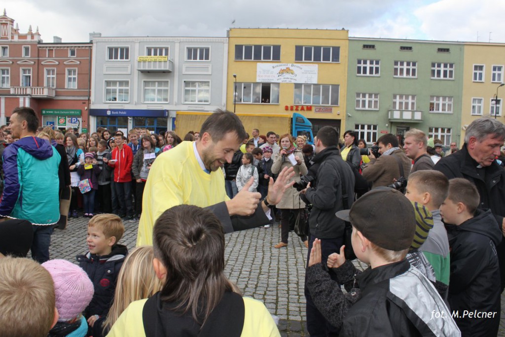 Tłum ludzi zgromadził się na placu miejskim, w centrum wydarzenia stoi mężczyzna w żółtej koszuli.