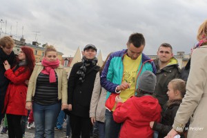 Grupa osób stoi na zewnątrz, w tle widoczne budynki i niebo z chmurami.