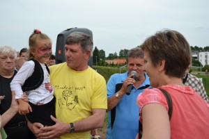 Mężczyźni rozmawiają z kobietą podczas wydarzenia plenerowego, przy dźwiękowni i z dzieckiem z malowanym policzkiem.