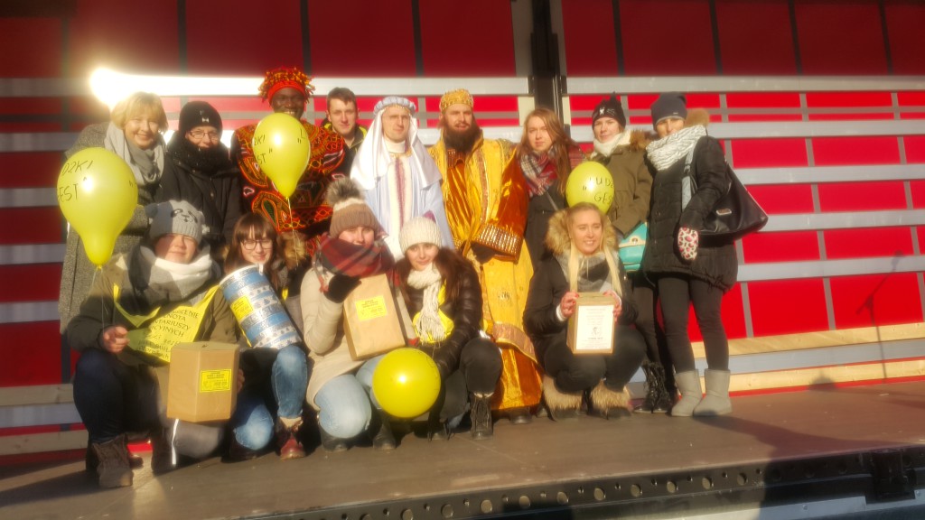 Grupa osób w strojach i z paczkami uczestniczy w kweście podczas Orszaku Trzech Króli.