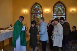 Uroczystość religijna w kościele, z udziałem księdza i wiernych, w tle widoczne witraże.