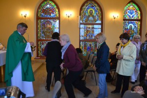 Uroczystość religijna w budynku z witrażami, na pierwszym planie kapłan odprawia ceremonię.