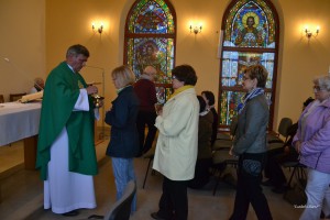Uroczystość religijna w kościele: kapłan udziela błogosławieństwa wiernym w obecności witraży.
