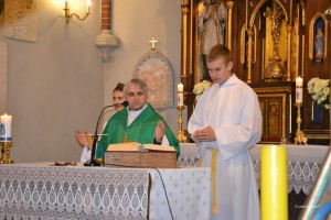 Dwóch mężczyzn podczas ceremonii wewnątrz kościoła, w otoczeniu ołtarza i świec.