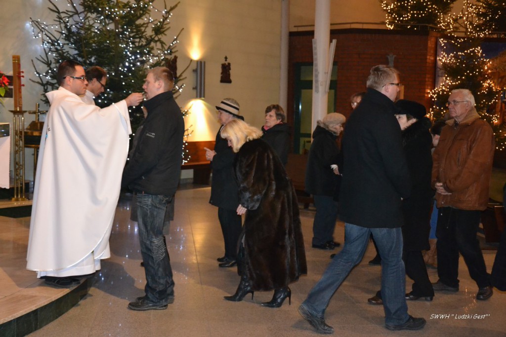Uroczystość w kościele, w tle choinka ozdobiona lampkami, uczestnicy wchodzą do środka.