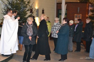 Uroczystość w budynku hospicjum, w tle choinka ozdobiona lampkami, obecny ksiądz i uczestnicy.