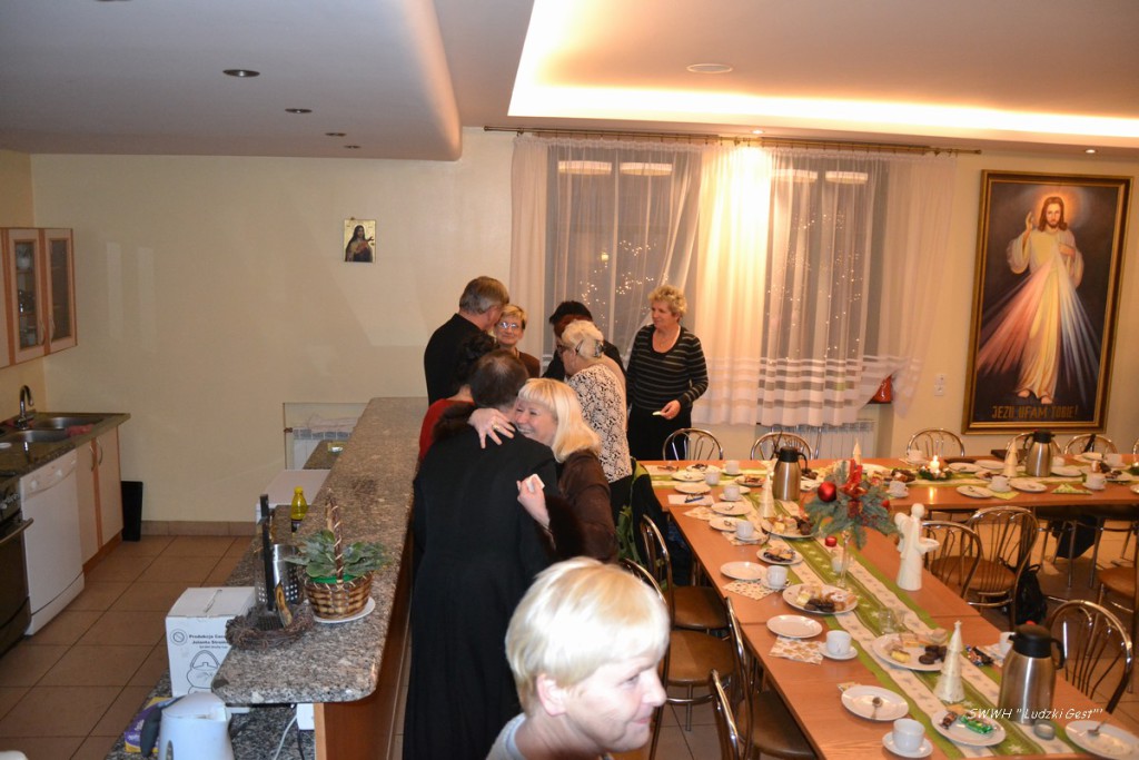 Grupa osób stoi przy długim stole nakrytym na uroczystość w jasnym pomieszczeniu.