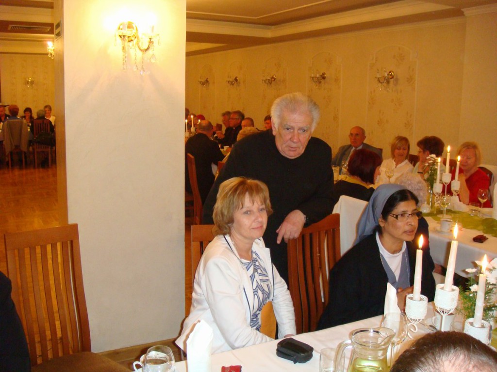Uczestnicy formalnej kolacji w elegancko urządzonej sali, widoczni w tle.