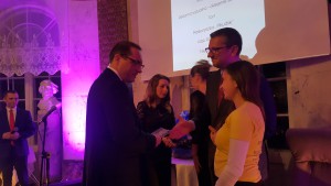 Uroczystość Noworoczna 2017: mężczyzna wręcza nagrodę osobie, w tle widoczny ekran z tekstem i dekoracje.