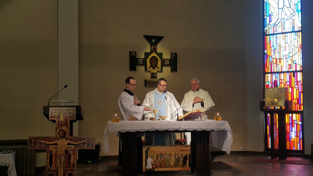 Trzej mężczyźni w szatach odprawiają liturgię przy ołtarzu w jasnym, bogato zdobionym wnętrzu kościoła.