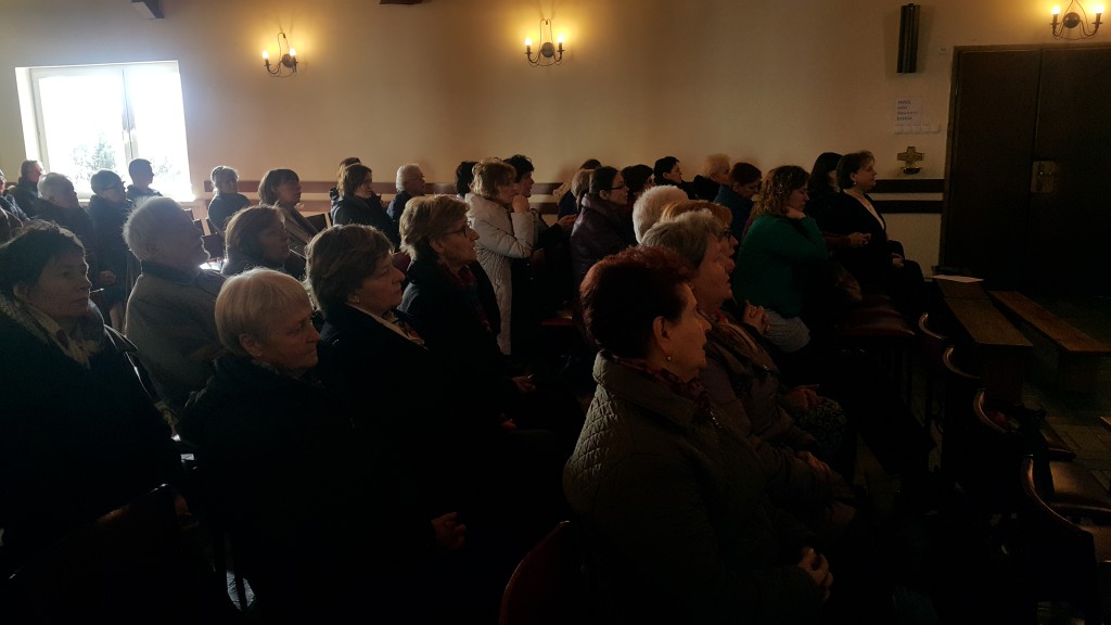 Grupa osób uczestniczy w Dniu Skupienia Wolontariatu Hospicyjnego w sali z oknami i lampami ściennymi.