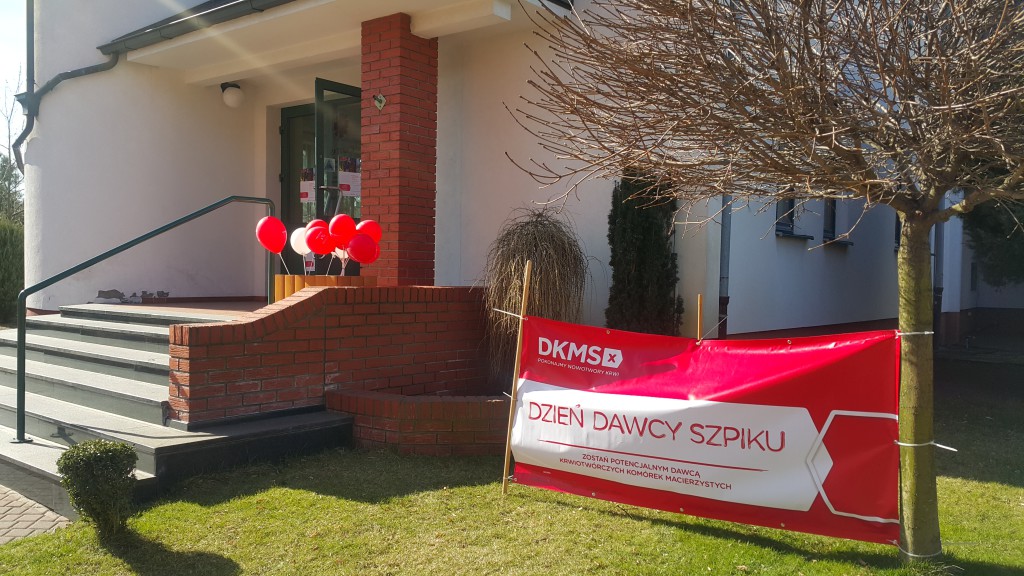 Budynek z czerwonymi ozdobami i banerem DKMS z napisem „Dzień Dawcy Szpiku”.