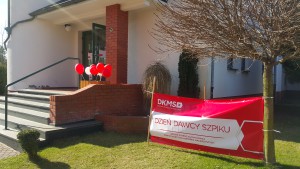 Budynek z czerwonymi ozdobami i banerem DKMS z napisem „Dzień Dawcy Szpiku”.